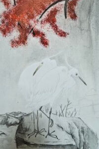 Zwei weiße Reiher stehen auf einem Felsen unter einem dichten, rot gefärbten Herbstbaum.