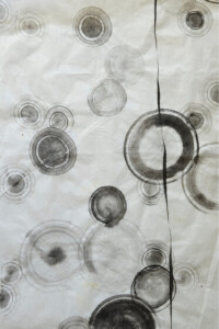 Kreisförmige schwarze und graue Ringe breiten sich in feiner Tuschemalerei auf hellem Grund aus, ein modernes Sumi-e Spiel der Formen.